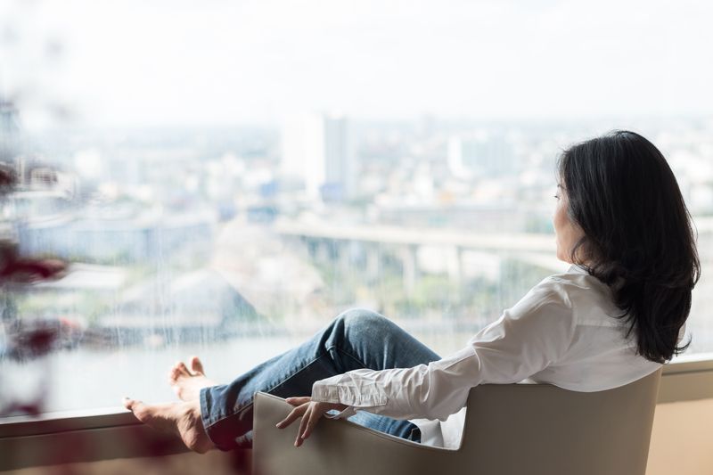 A woman is sitting in a chair looking out of a window.