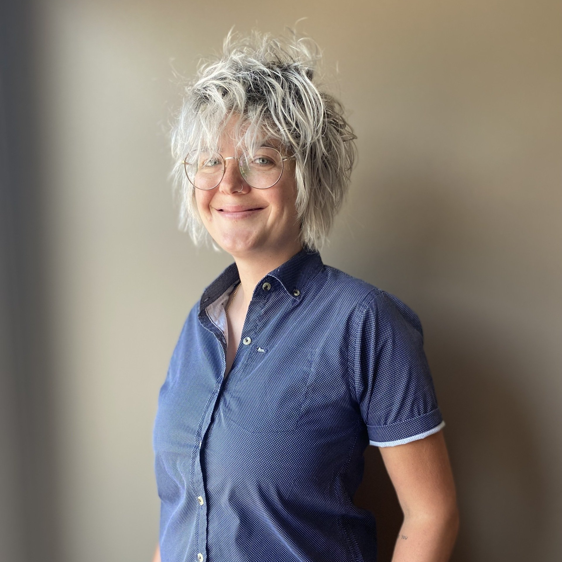 A woman wearing glasses and a blue shirt is smiling for the camera.