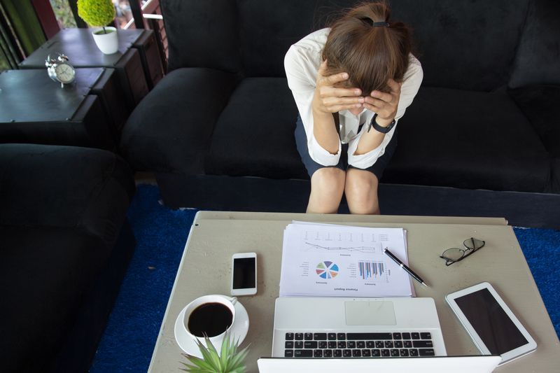A woman is sitting on a couch with her head in her hands.