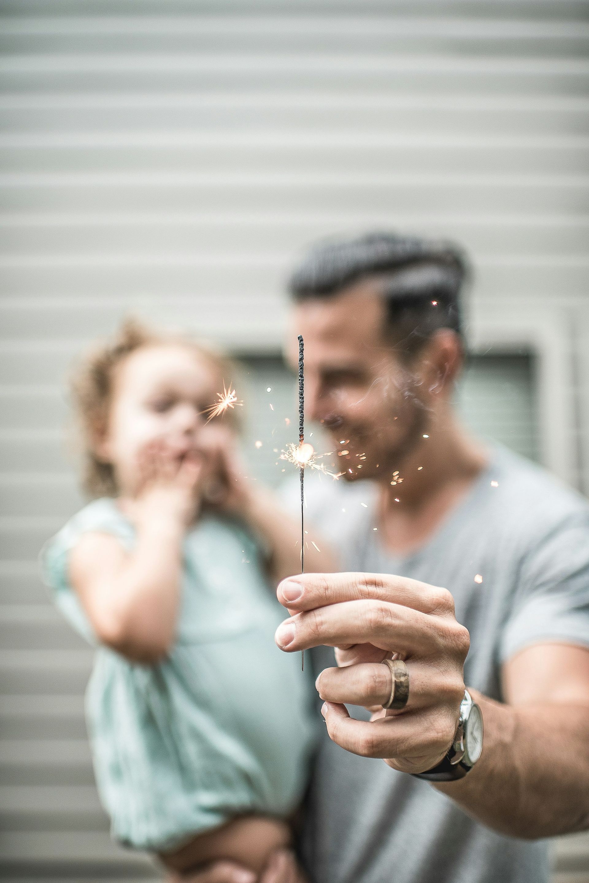 Father holding a sparkler with a small child in his arms, both watching sparks fly.