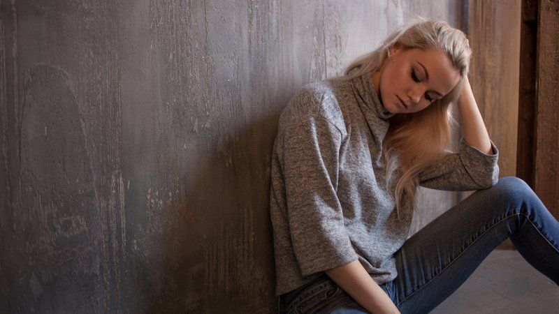 A woman is sitting on the floor leaning against a wall.