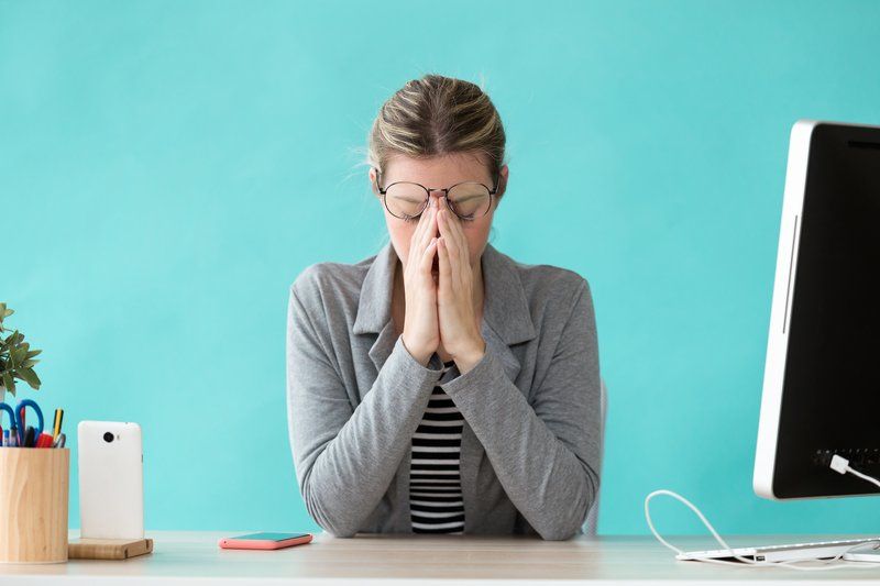A woman is sitting at a desk with her hands on her face.