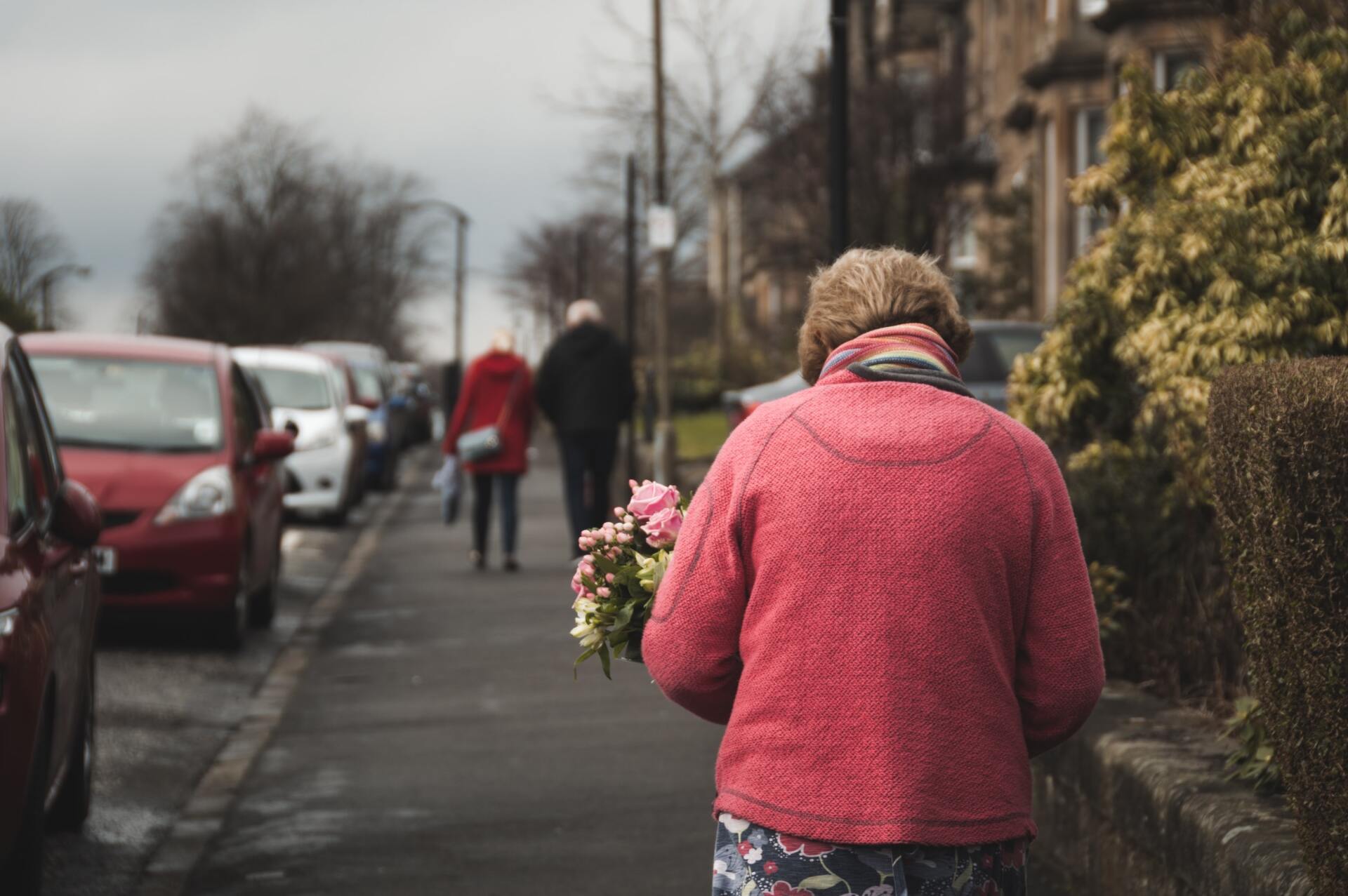 An elderly woman is walking down the street holding a bouquet of flowers.
