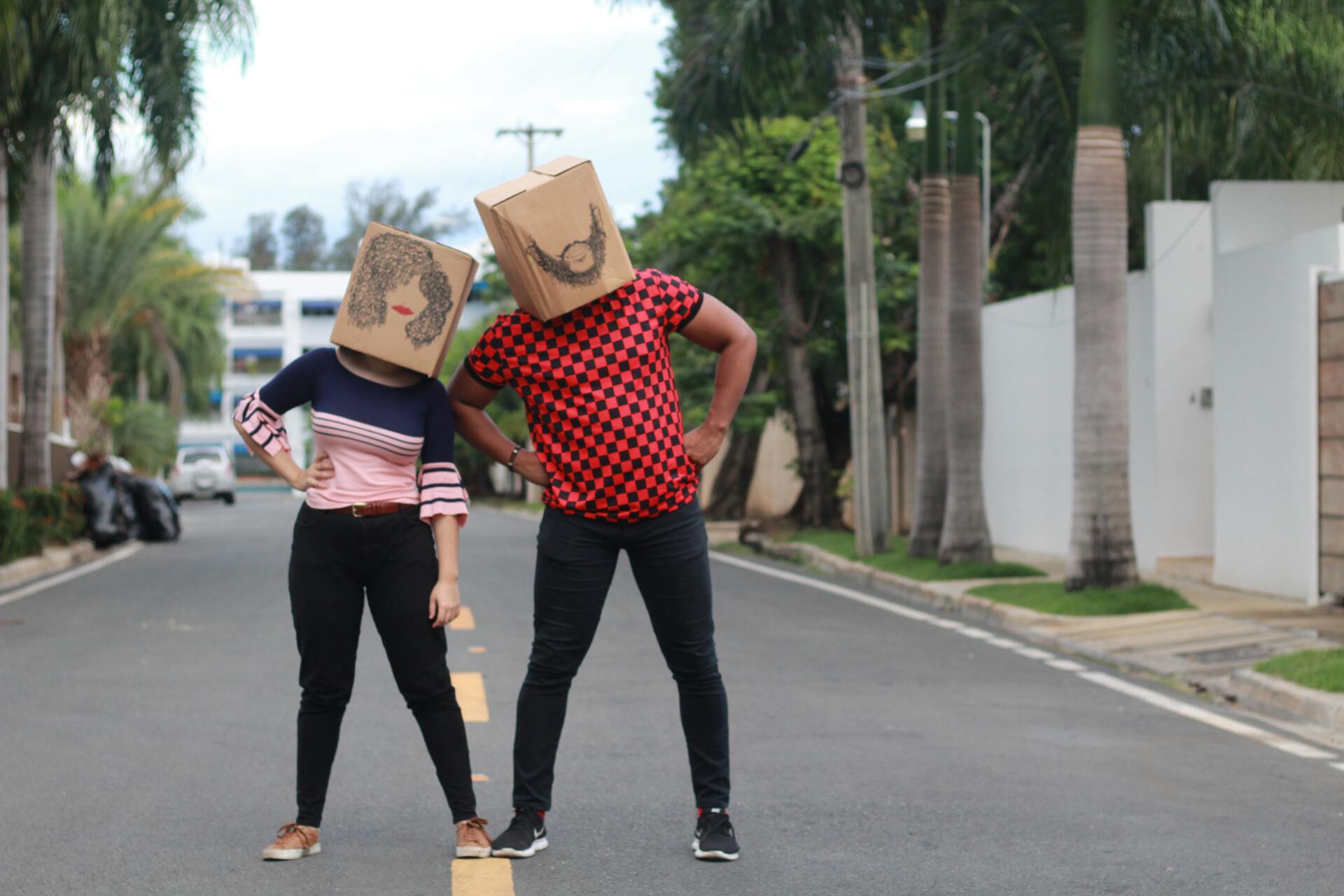 A man and a woman are standing on a street with cardboard boxes on their heads.