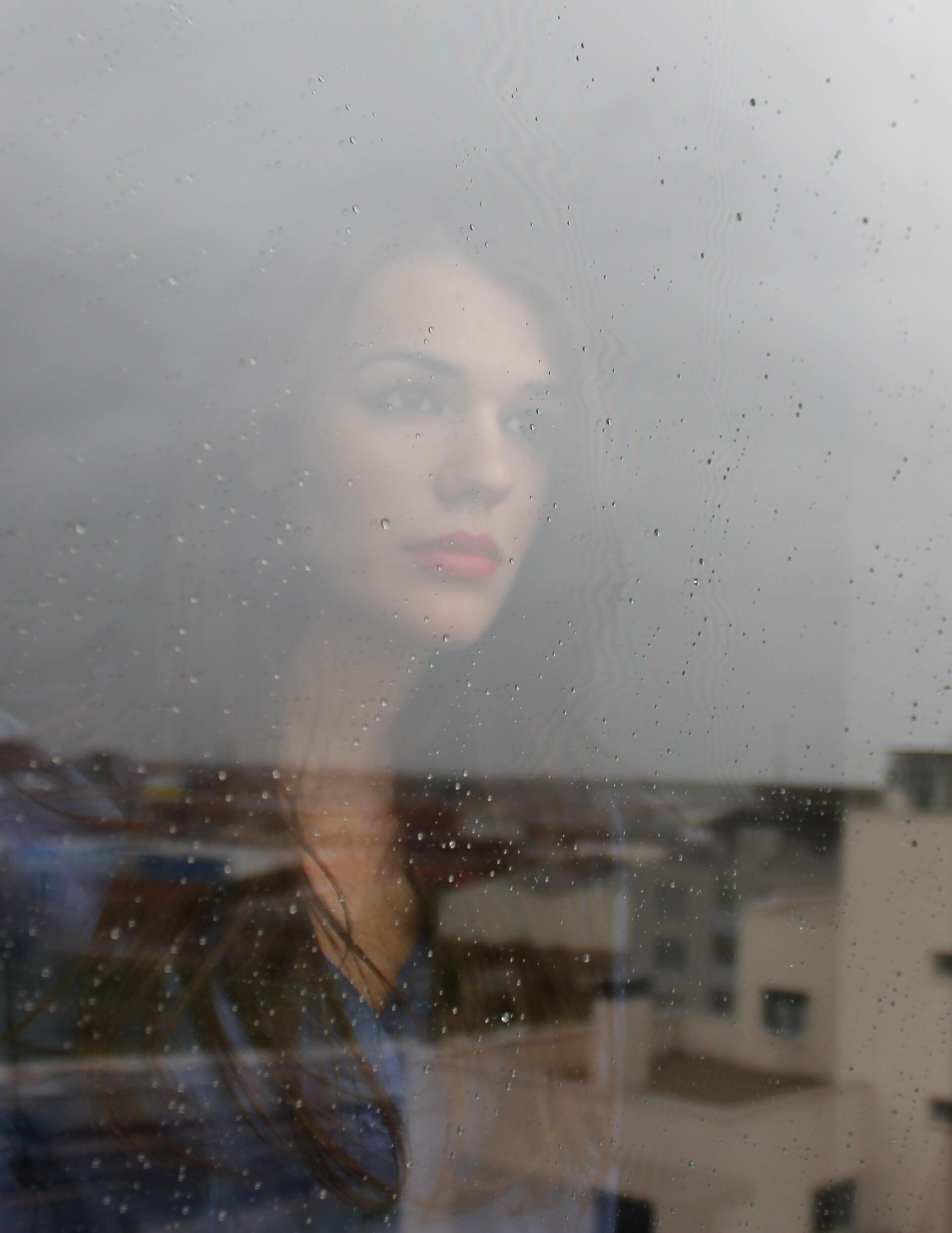 A woman is looking out of a window on a rainy day.