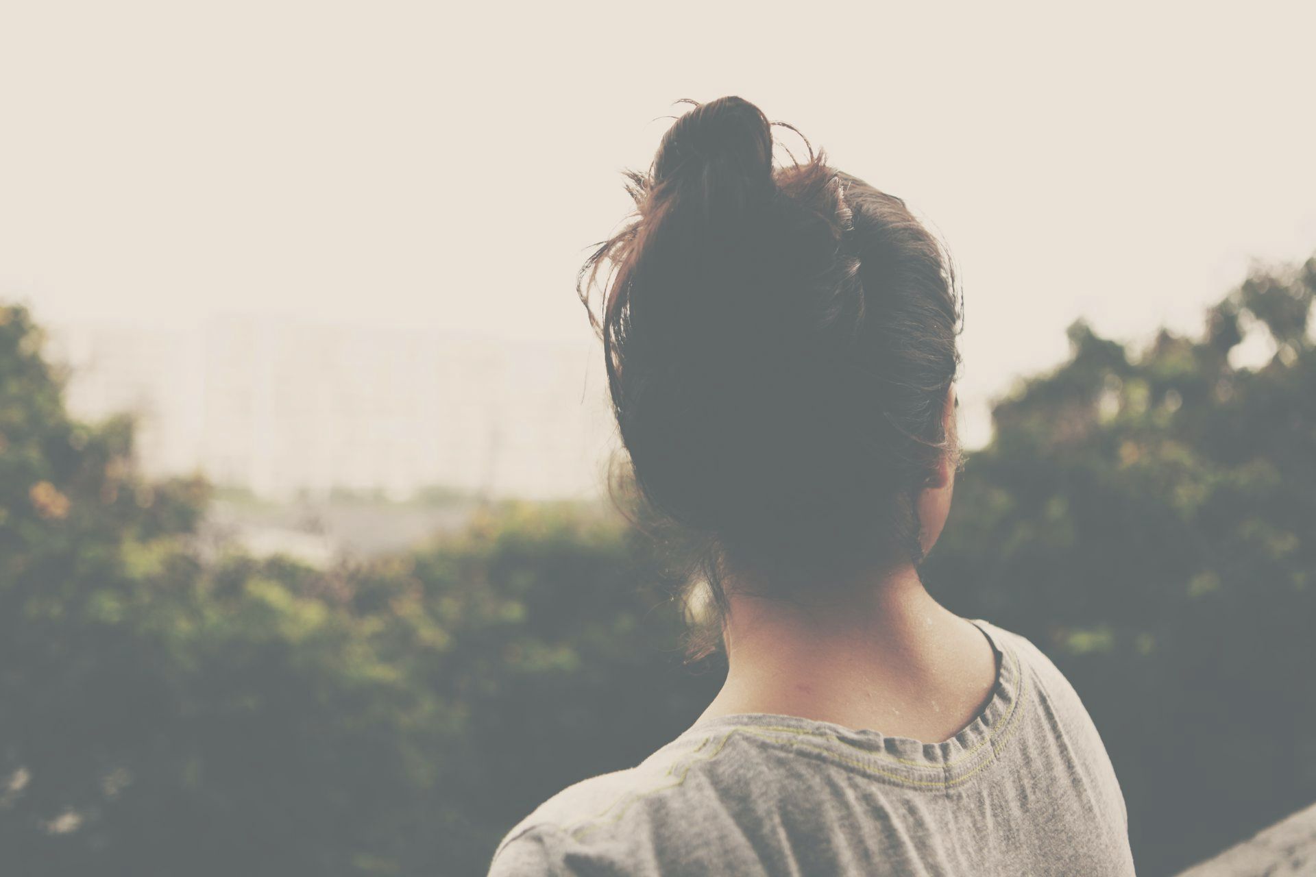 A woman with her hair in a bun is standing in front of trees.