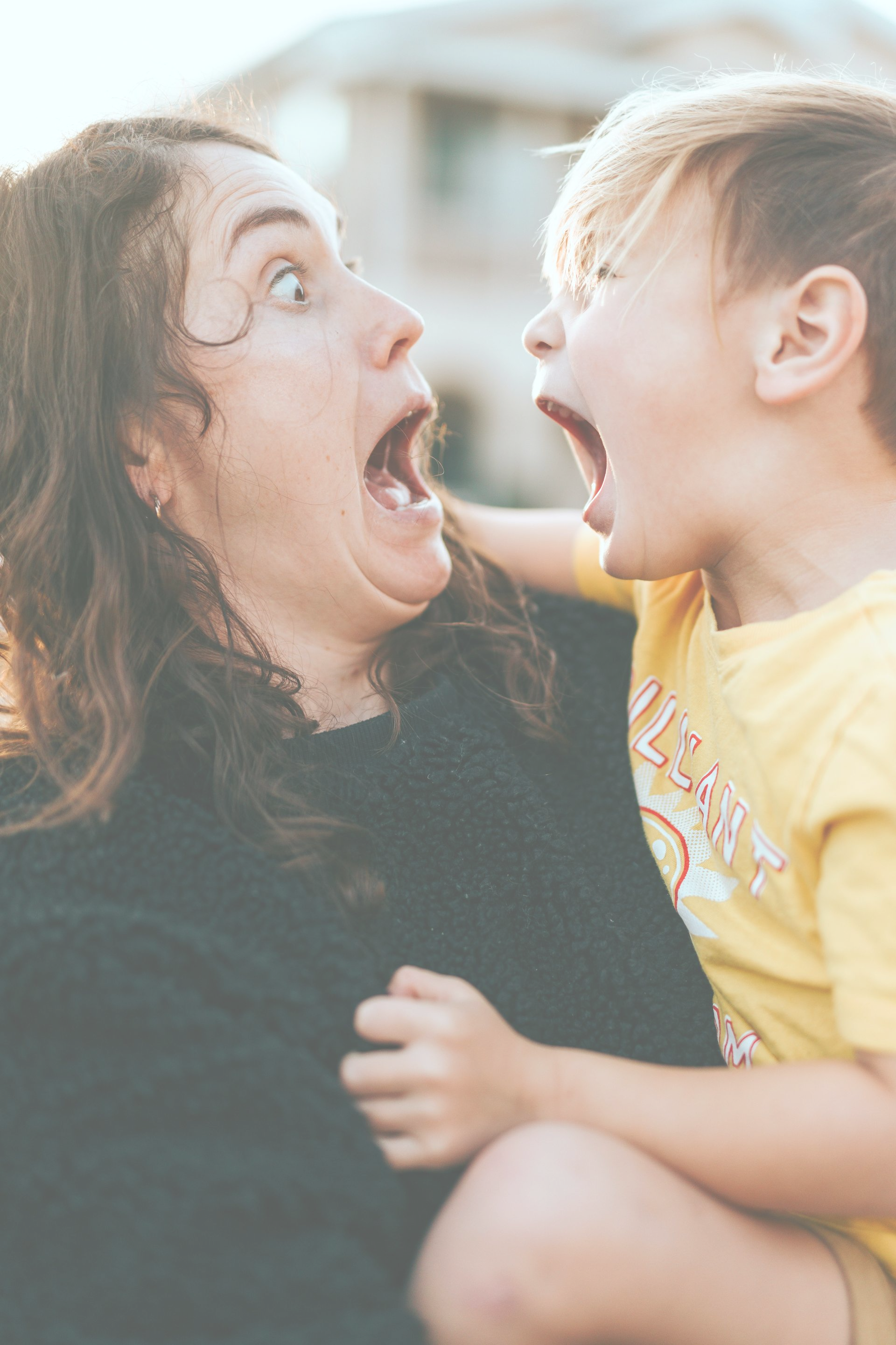 A person in a dark sweater and a child in a yellow shirt with their mouths open, mirroring each other's expressions.