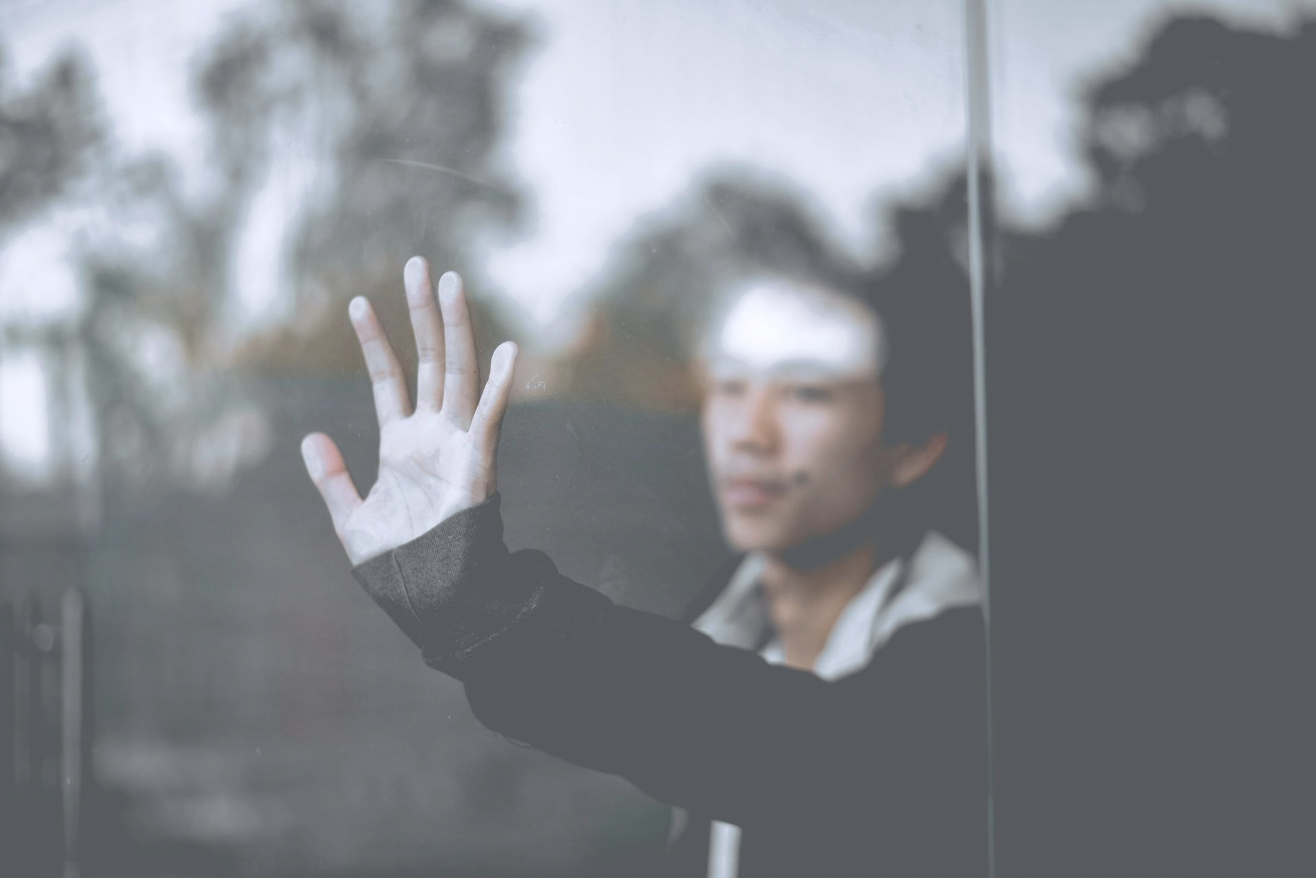 A person reaches out with an open hand against a glass surface, their face slightly out of focus in the background.