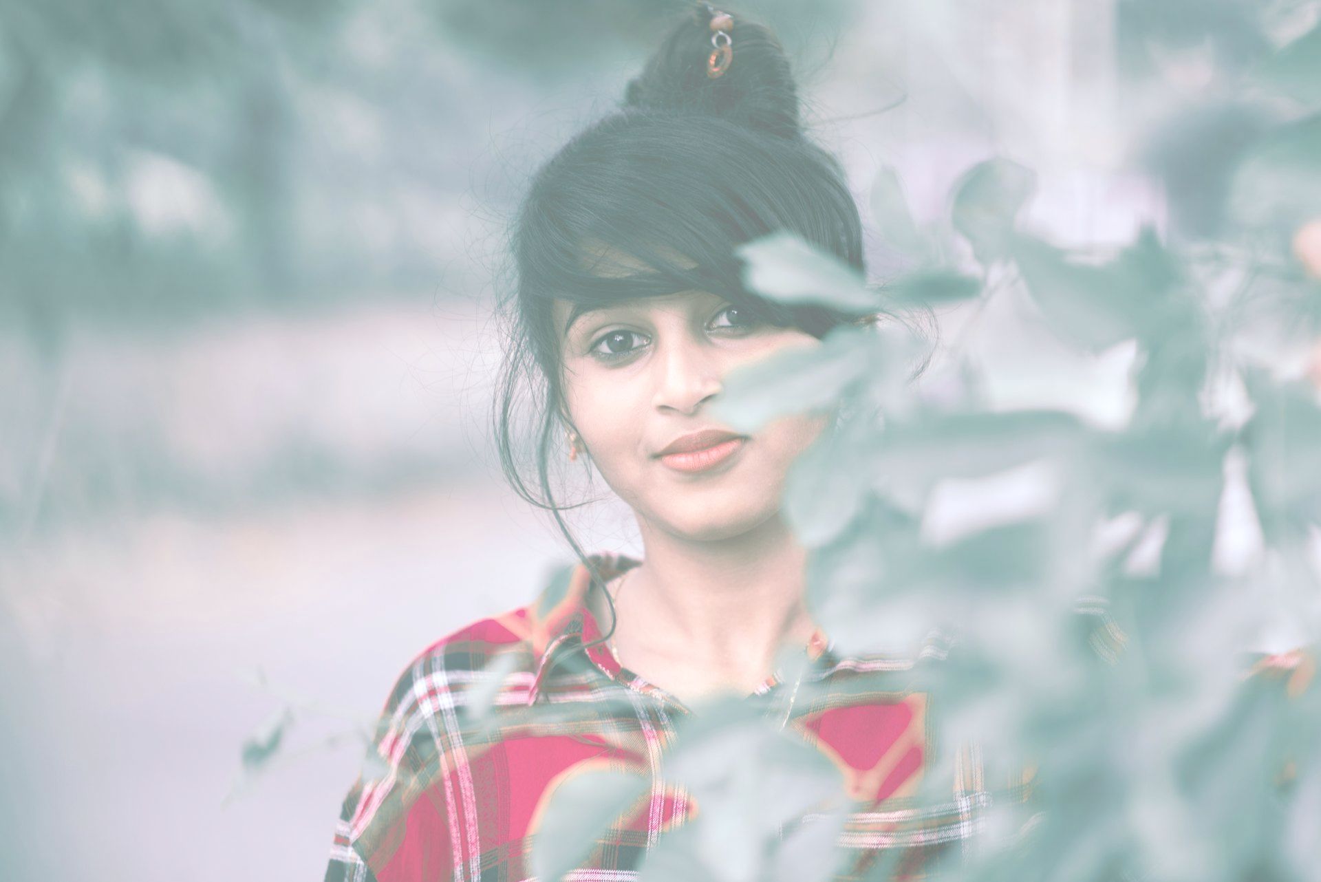 A young woman in a plaid shirt is standing in front of a tree.