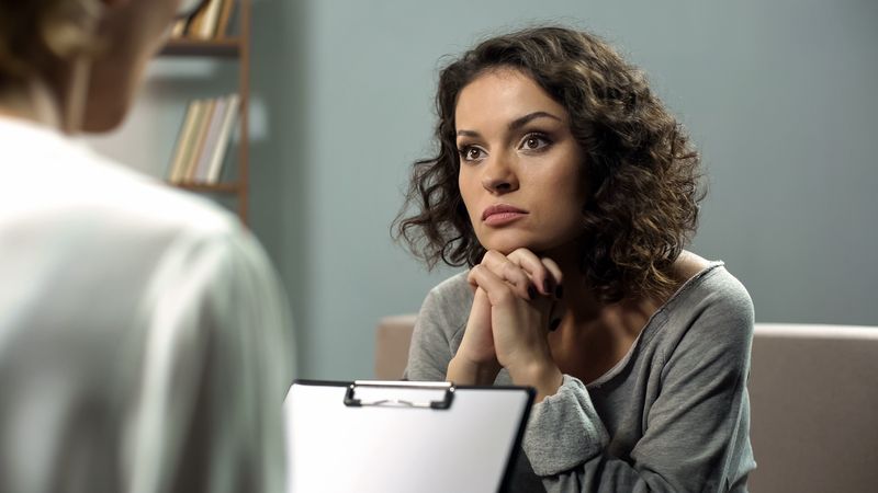 A woman is sitting on a couch talking to a doctor.