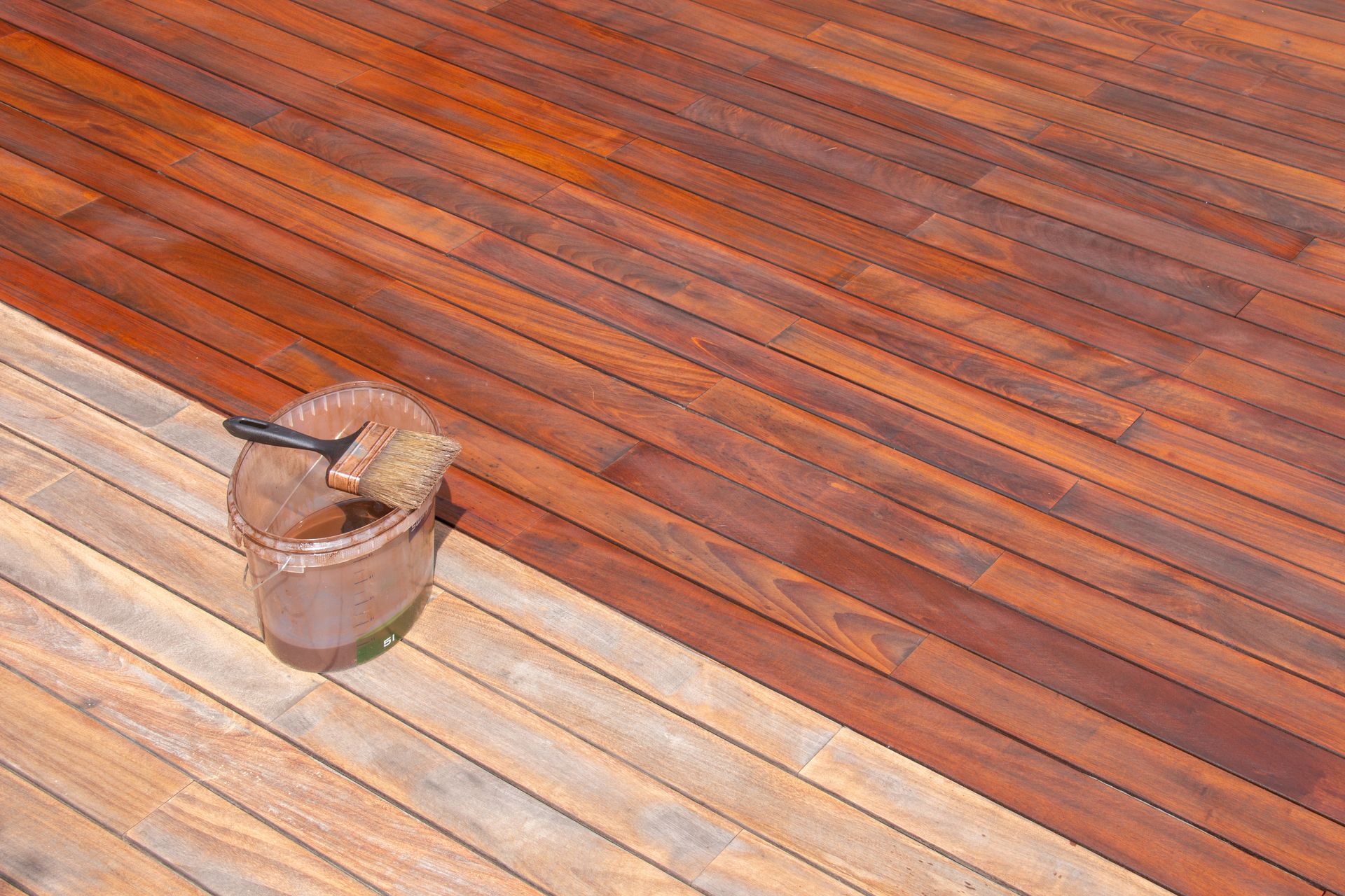 Bucket on a sunlit wooden deck with a diagonal pattern of reddish and pale planks