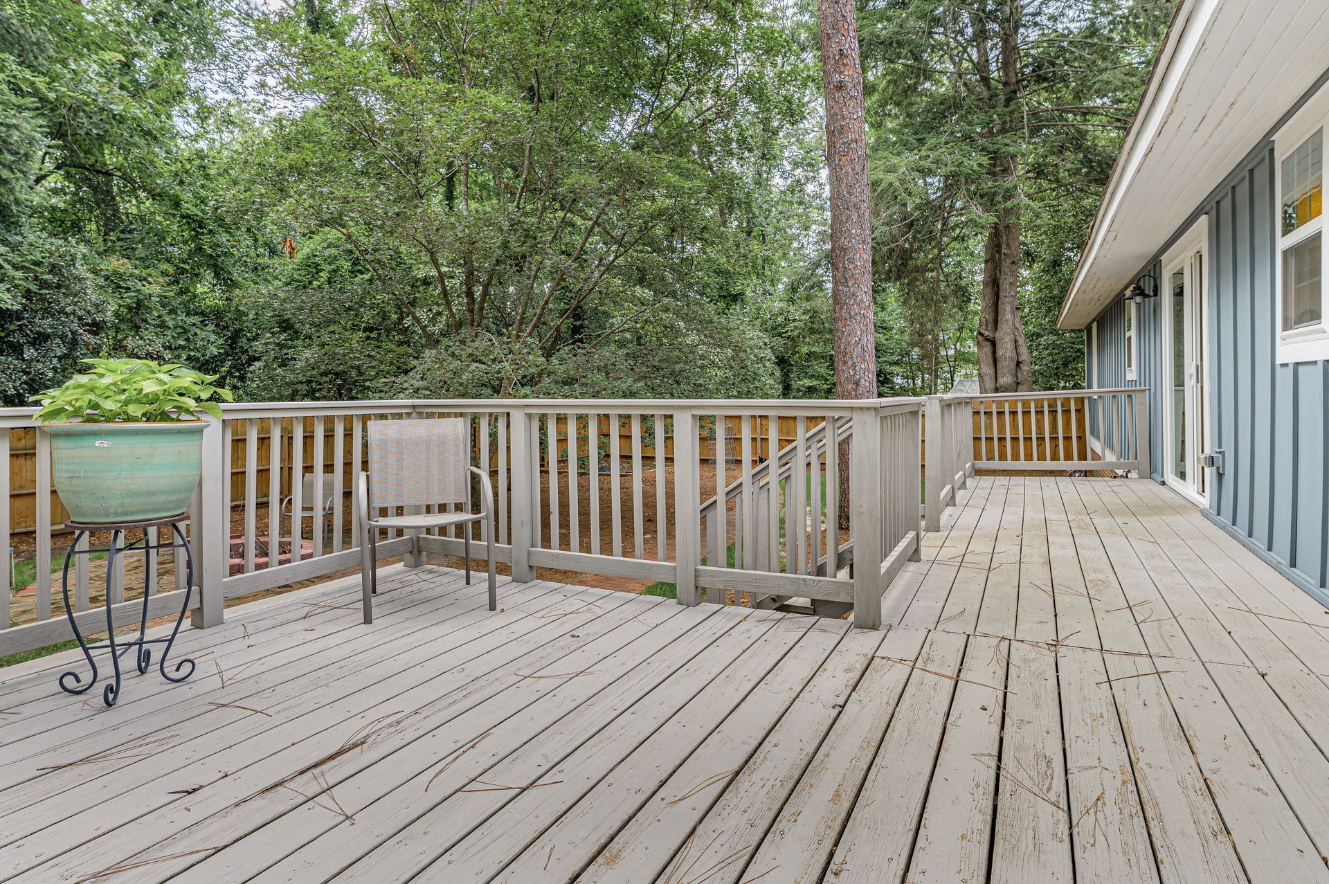 Wooden backyard deck with railing, blue house siding, and trees beyond.