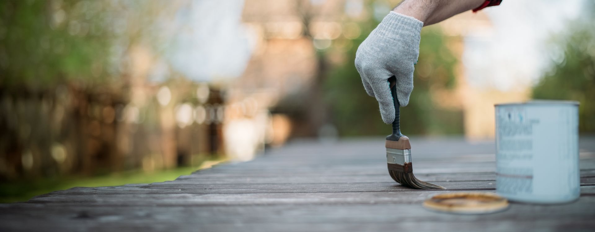 Gloved hand painting a line on a wooden surface beside a white paint can outdoors