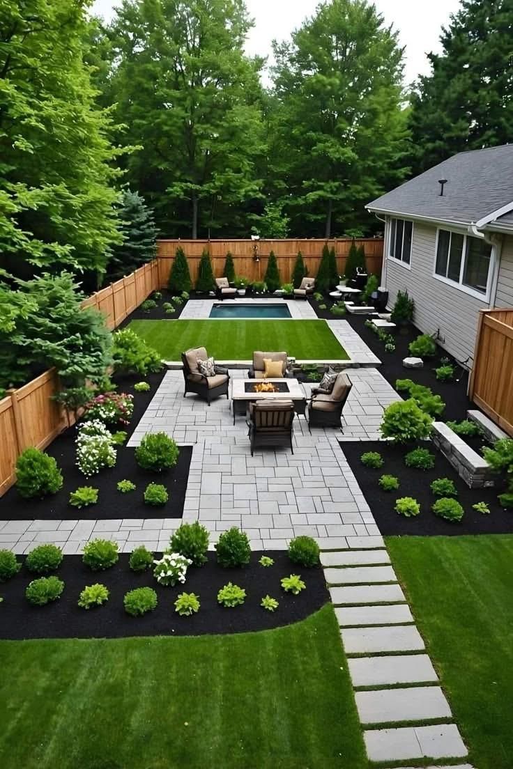 Landscaped backyard patio with fire pit, pool, stone path, and wooden fence surrounding lush greenery