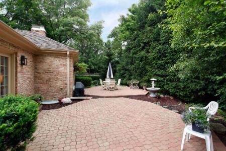 Brick patio with outdoor seating, umbrella, and lush green backyard trees