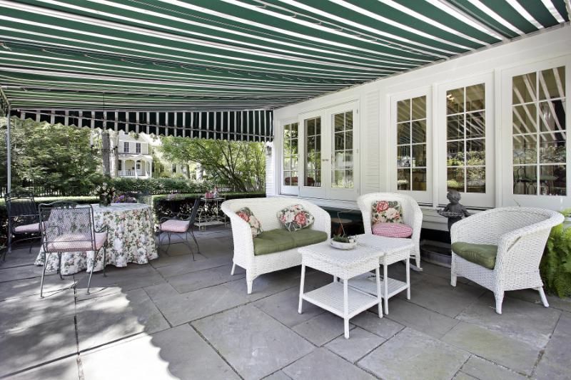 Covered patio with striped awning, white wicker furniture, and a round table over stone flooring