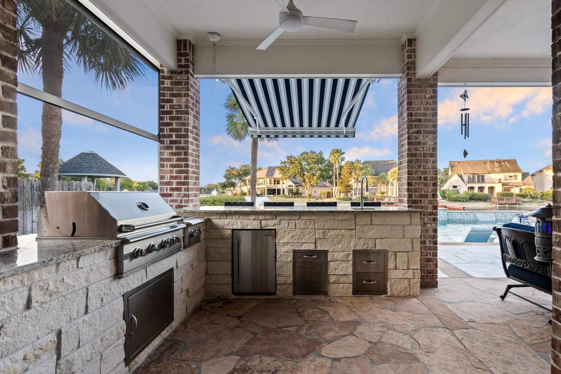 Covered outdoor patio kitchen with grill, counter seating, and a pool view beyond the open windows