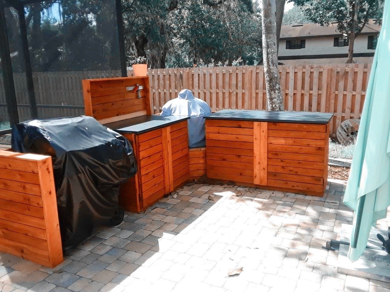 Backyard patio with orange wooden planter boxes, black covered items, and a paved seating area