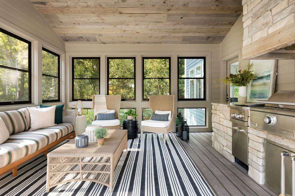 Bright sunroom with striped rug, woven sofa, coffee table, and large windows overlooking greenery