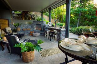 Covered patio with grill, seating, and a pool beyond, overlooking lush green trees