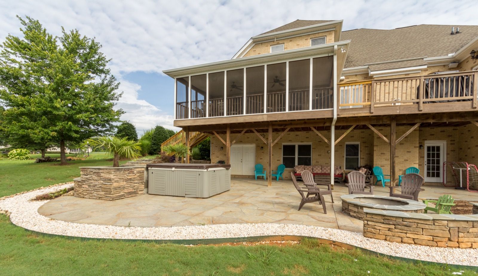 Backyard patio with stone house, screened porch, outdoor seating, and a landscaped lawn