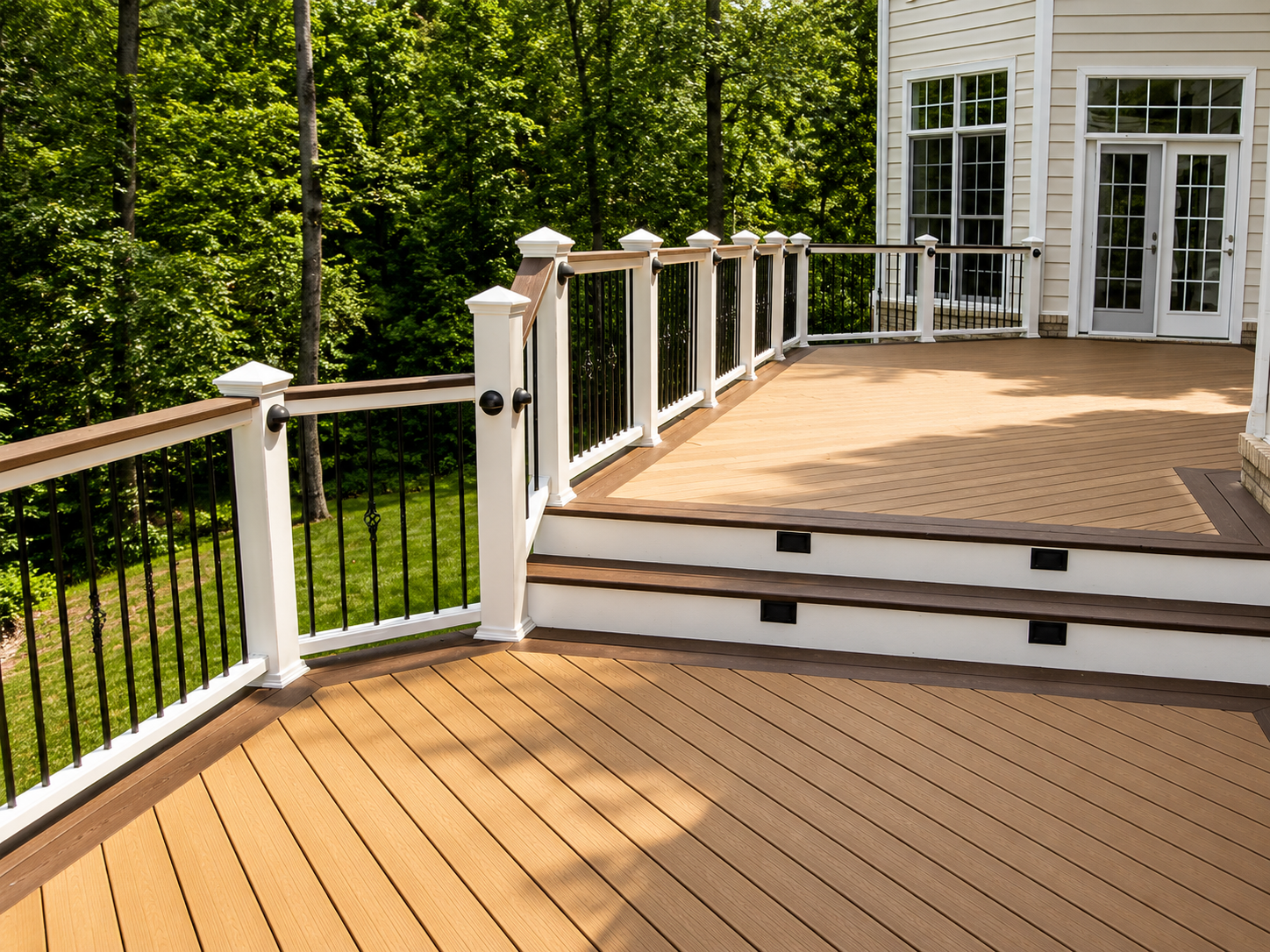 Wooden deck with white railings and steps leading to a house, bordered by green trees.