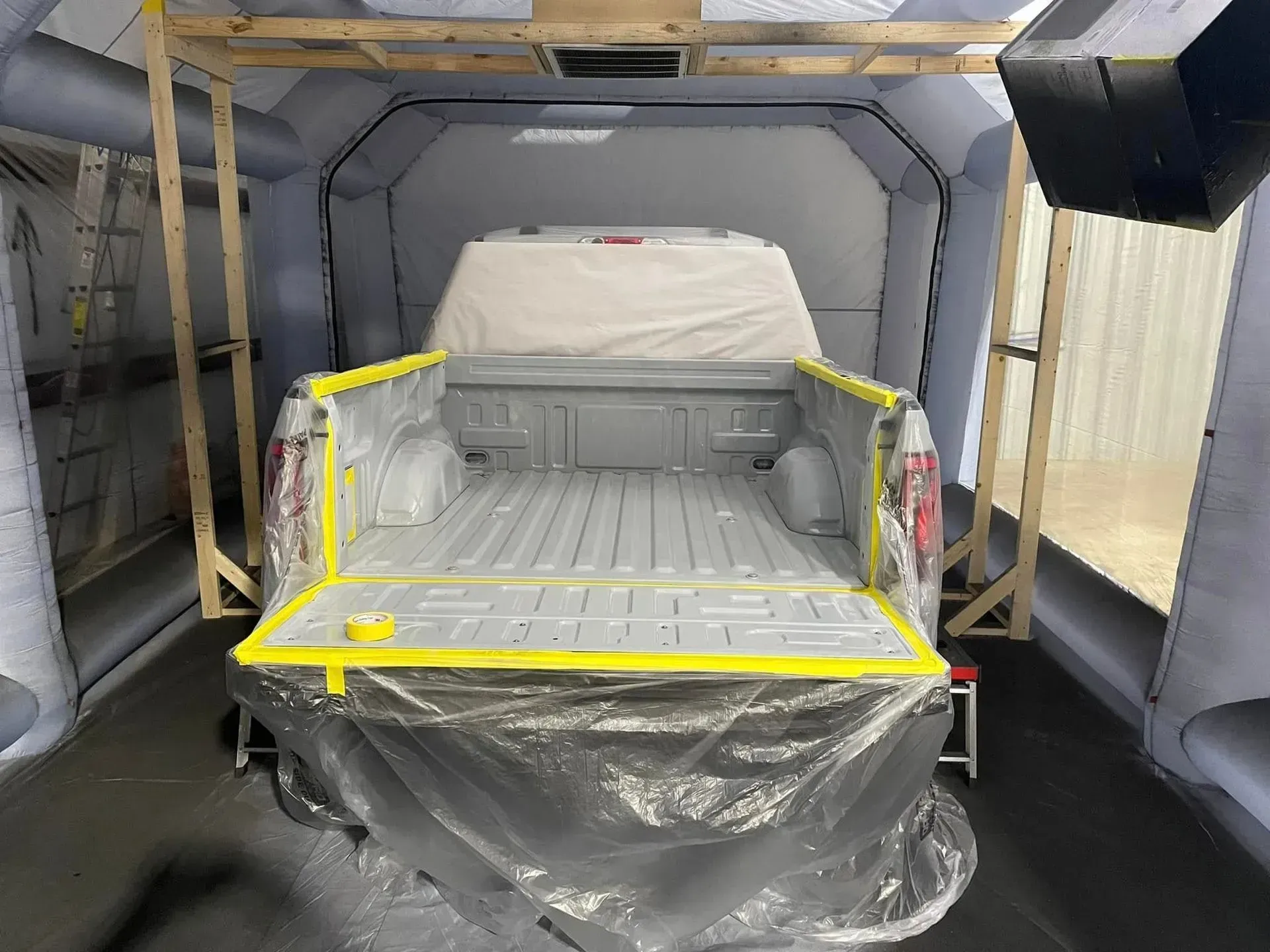 A pickup truck bed prepped for painting inside an enclosed paint booth.
