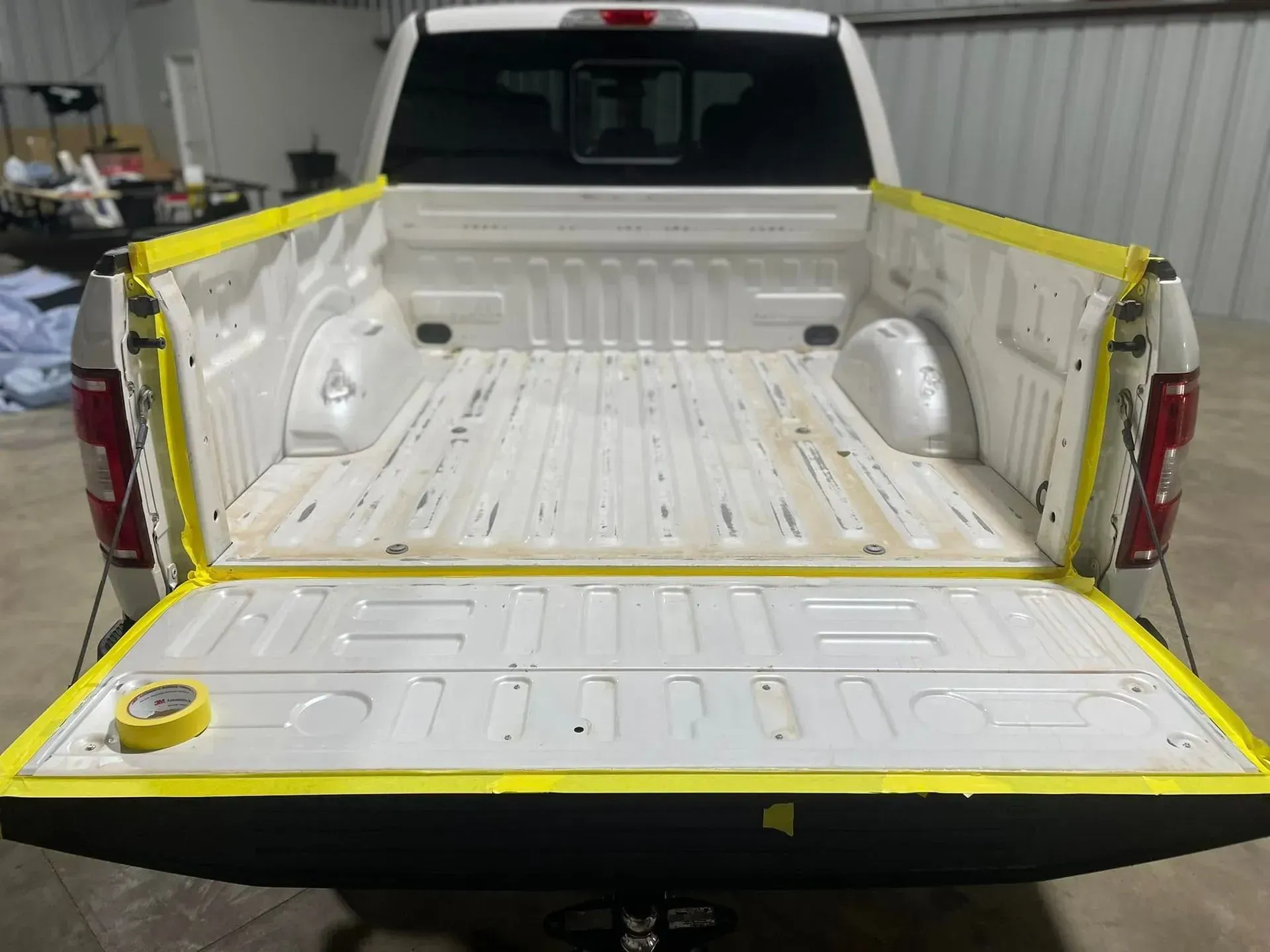 White truck bed with yellow tape masking the edges, ready for painting.