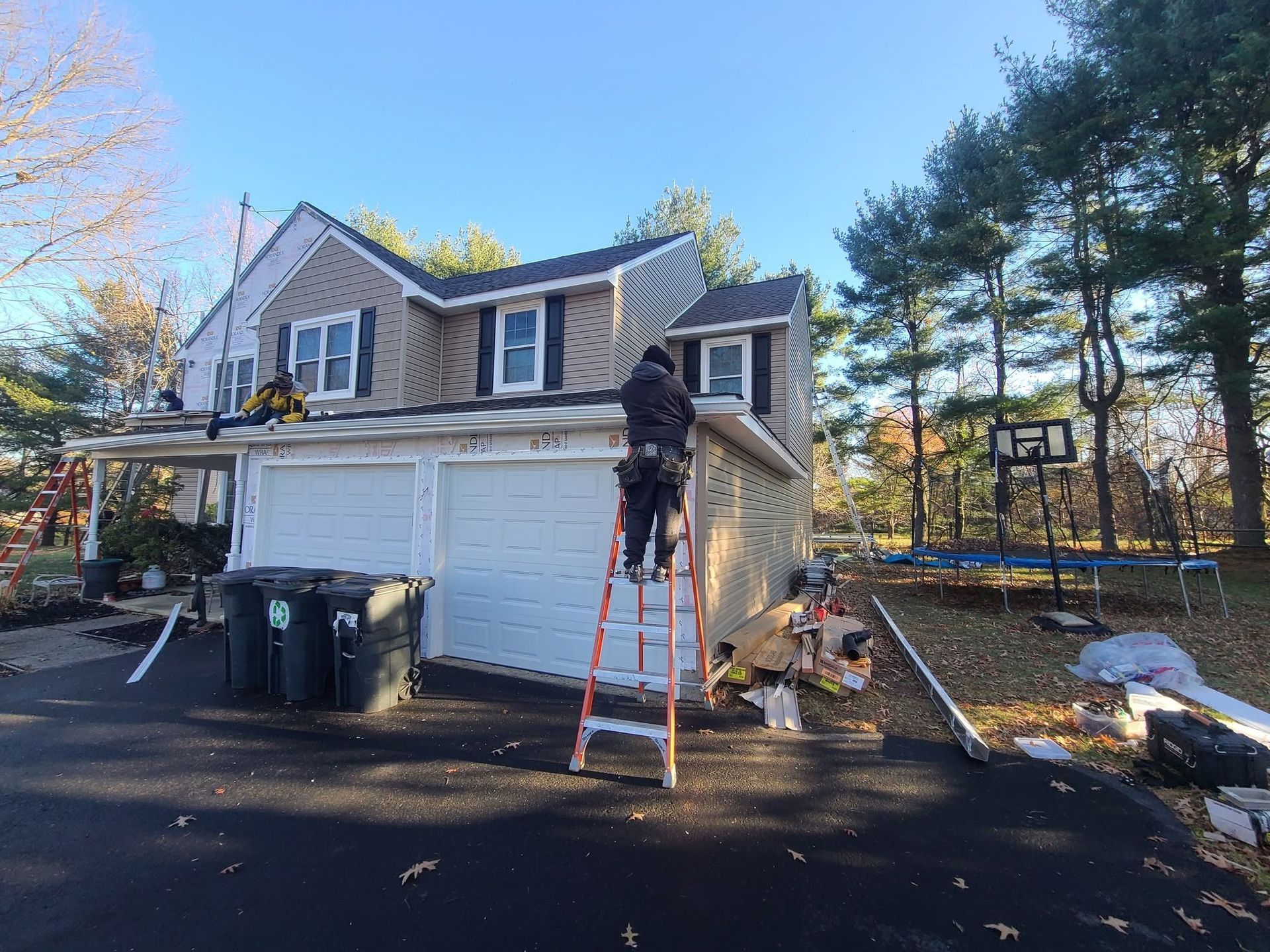 Person on ladder cleaning the white siding of a two-story house in a driveway.
