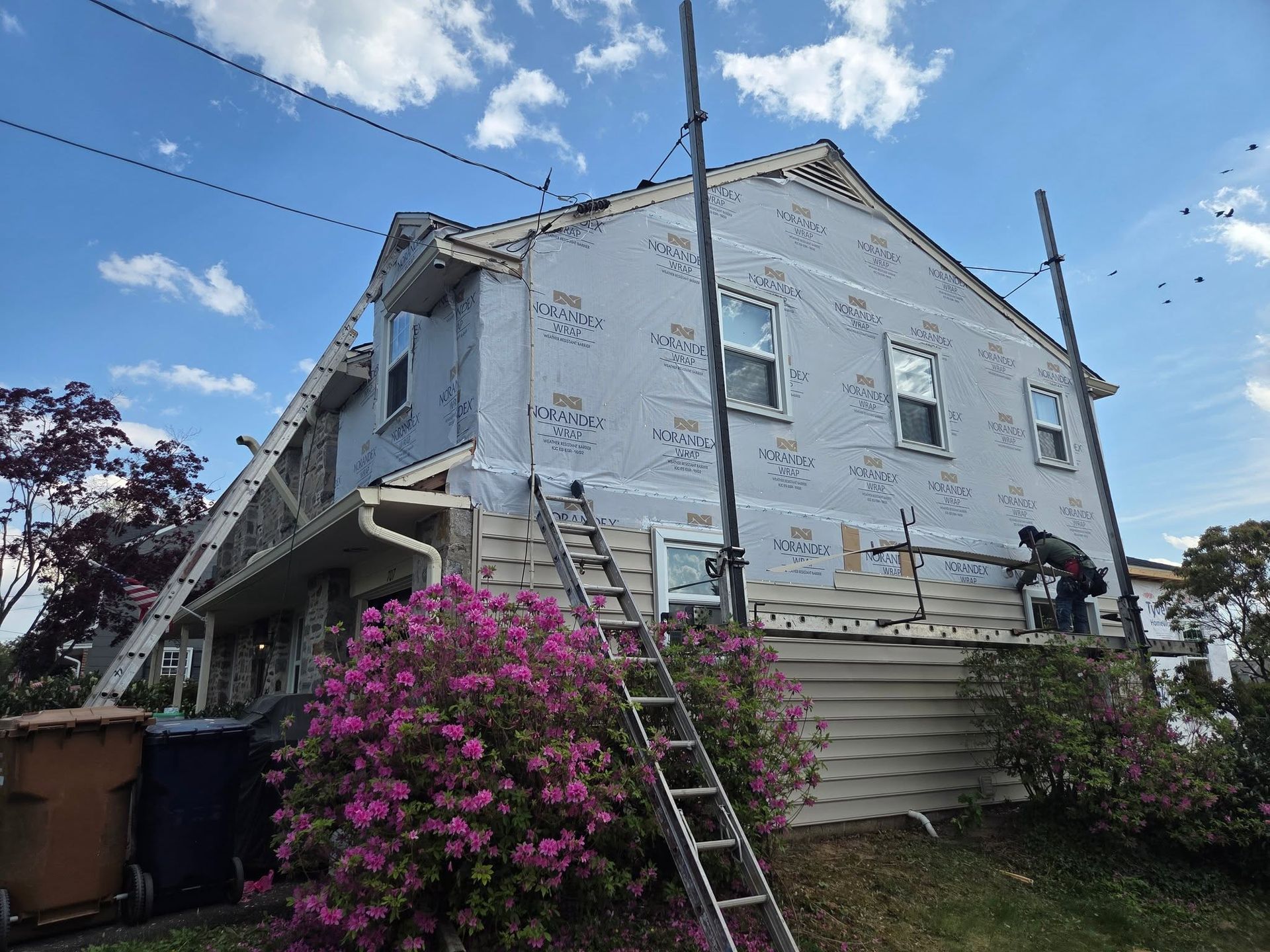 Weathered two-story house with peeling paint, exterior stairs, and pink flowering bushes in the yard
