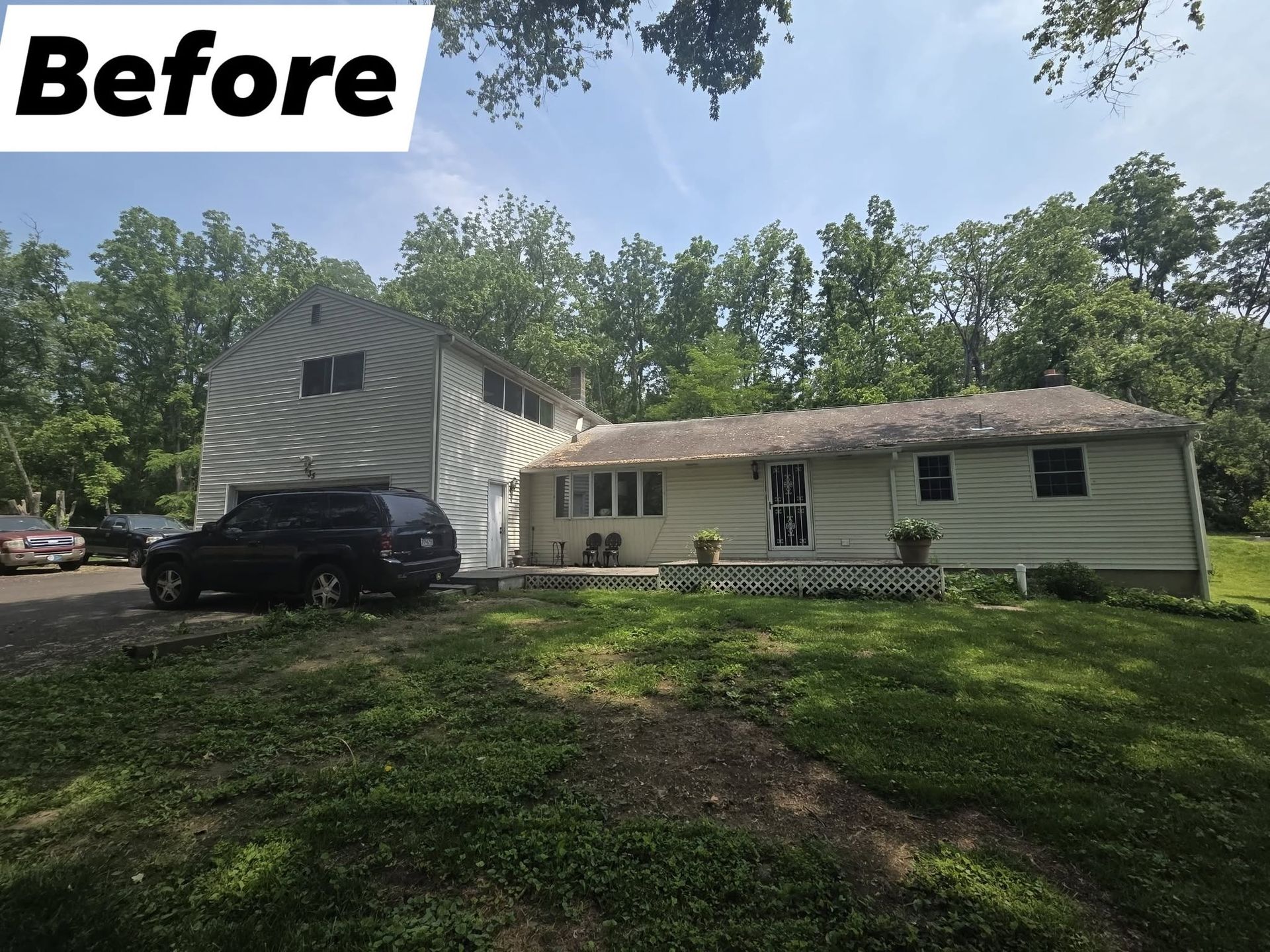Before photo of a white house with a dark roof and black SUV in a grassy yard under trees