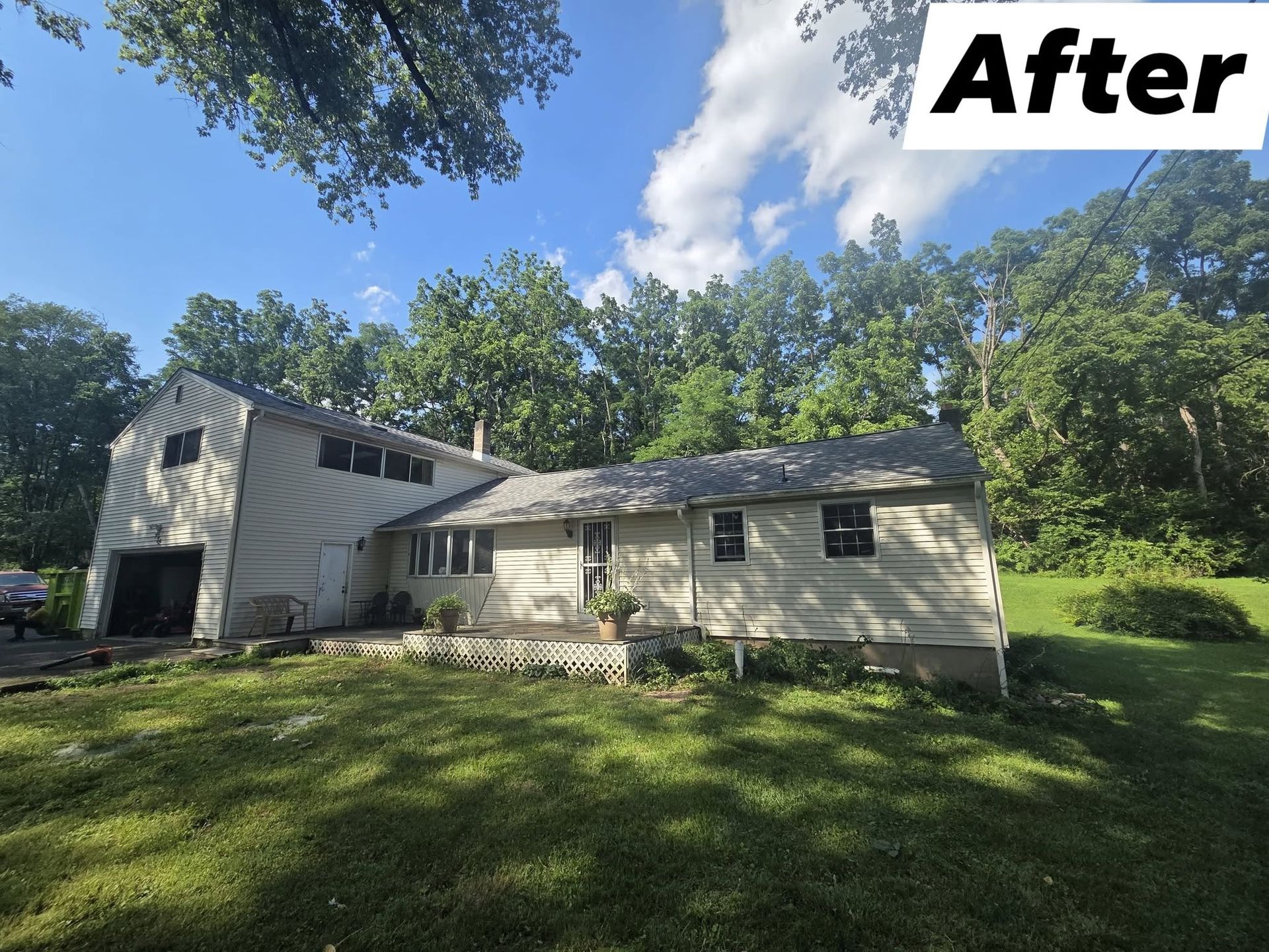 After photo of a beige house and attached garage in a grassy yard with trees and blue sky