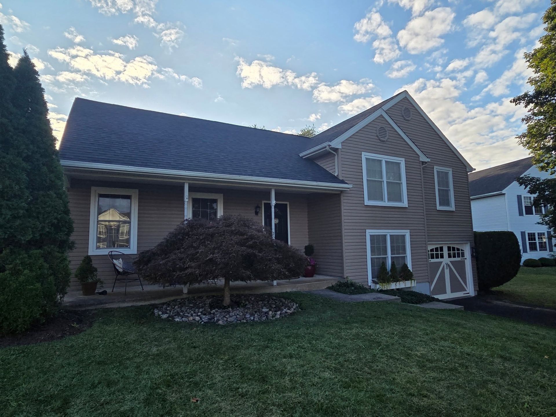 Suburban two-story house with gray siding, dark roof, white trim, and a green lawn at dusk.