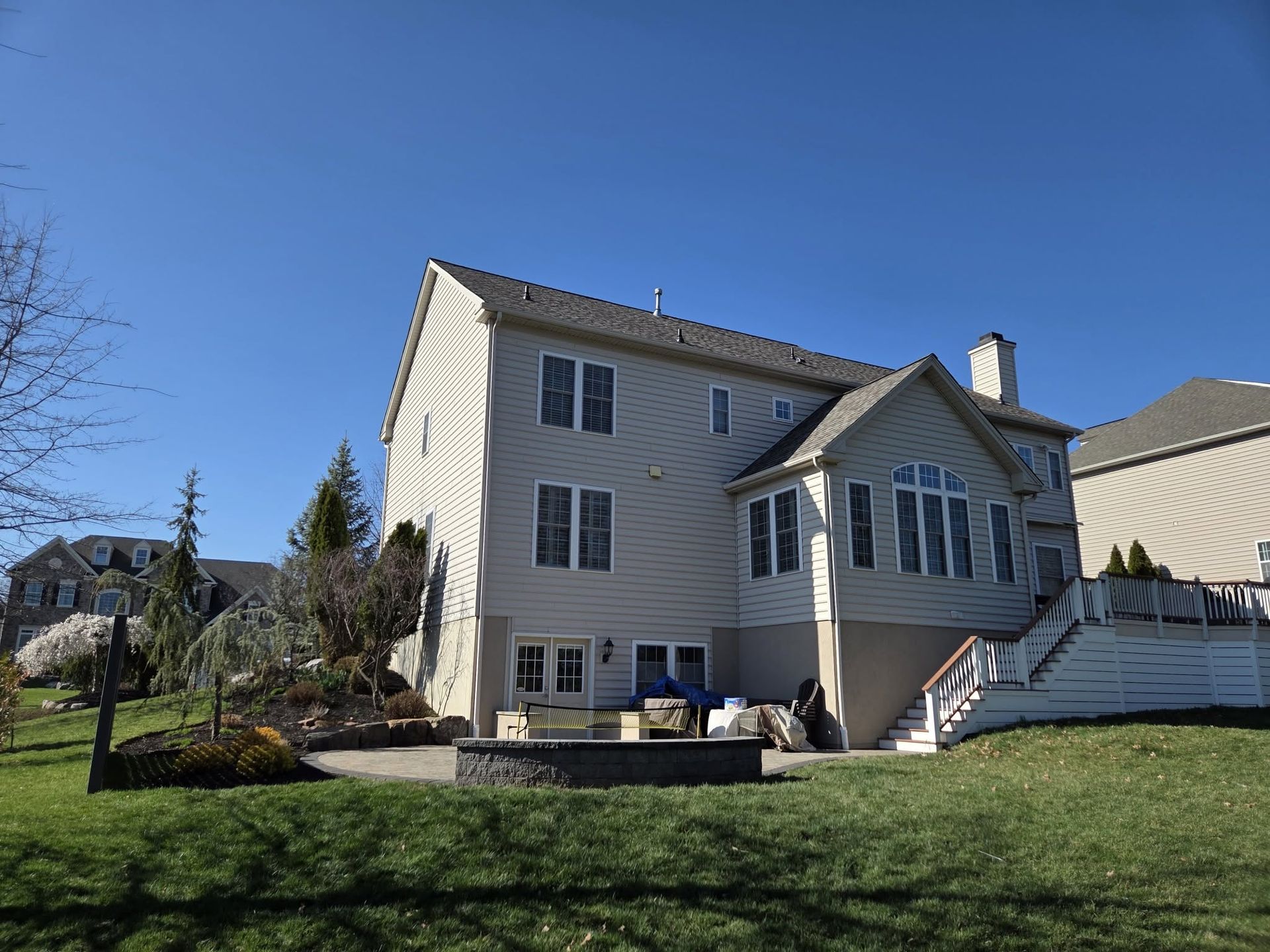 Suburban two-story beige house with white trim and a green lawn under a clear blue sky