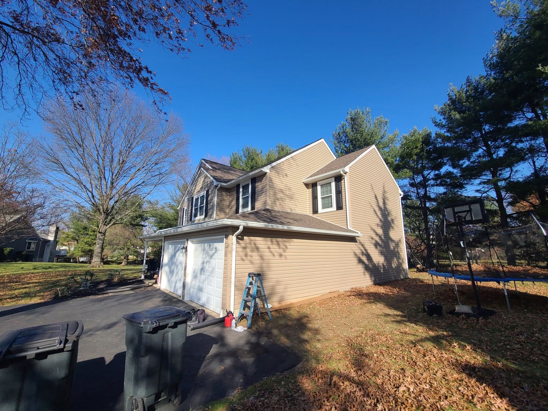 Suburban house with attached garage on a sunny day, framed by trees and a clear blue sky