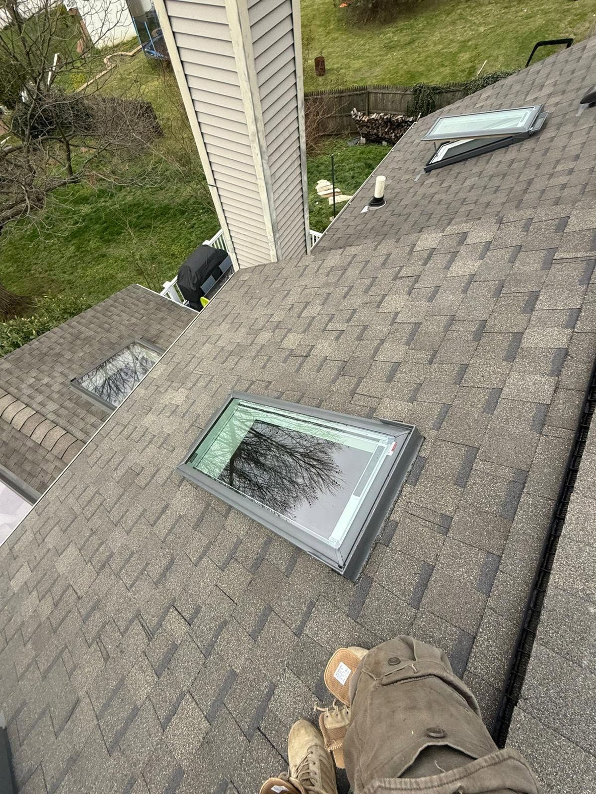 Roof with gray shingles, two skylights, and a chimney near a grassy yard below.