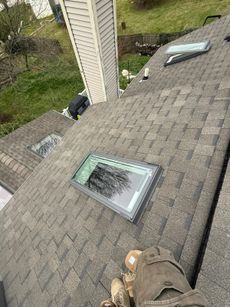 Rooftop with gray shingles, two skylights, and a small vent near a chimney in a grassy suburban area