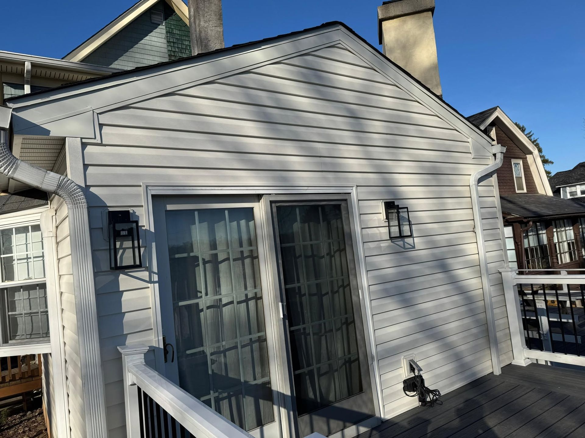 White-sided house exterior with sliding glass doors, wall lights, and a small deck under a blue sky