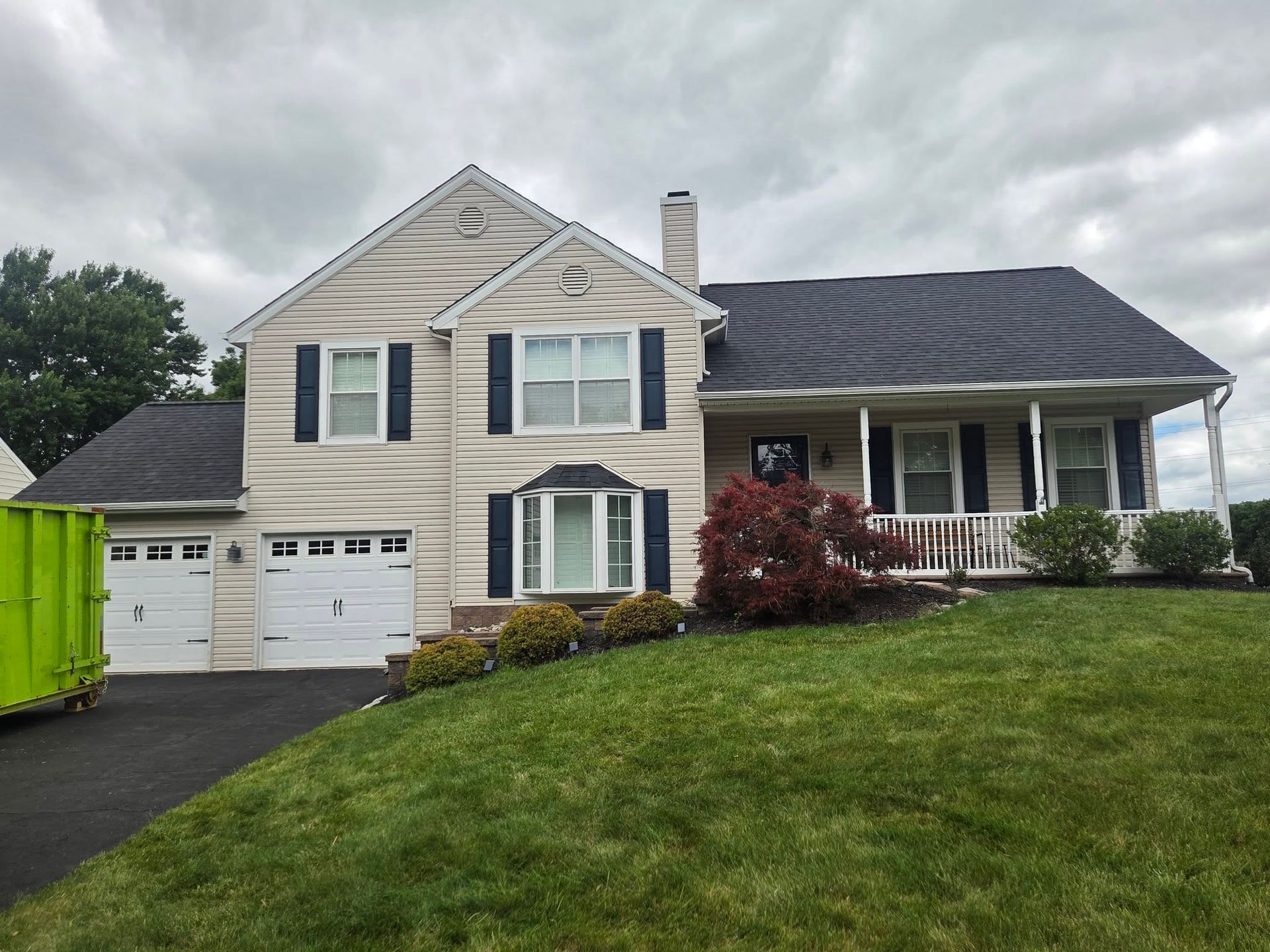 Suburban two-story beige house with garage, dark roof, front porch, and green lawn