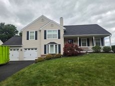 Suburban house with beige siding, white trim, attached garage, and front porch on a grassy hill