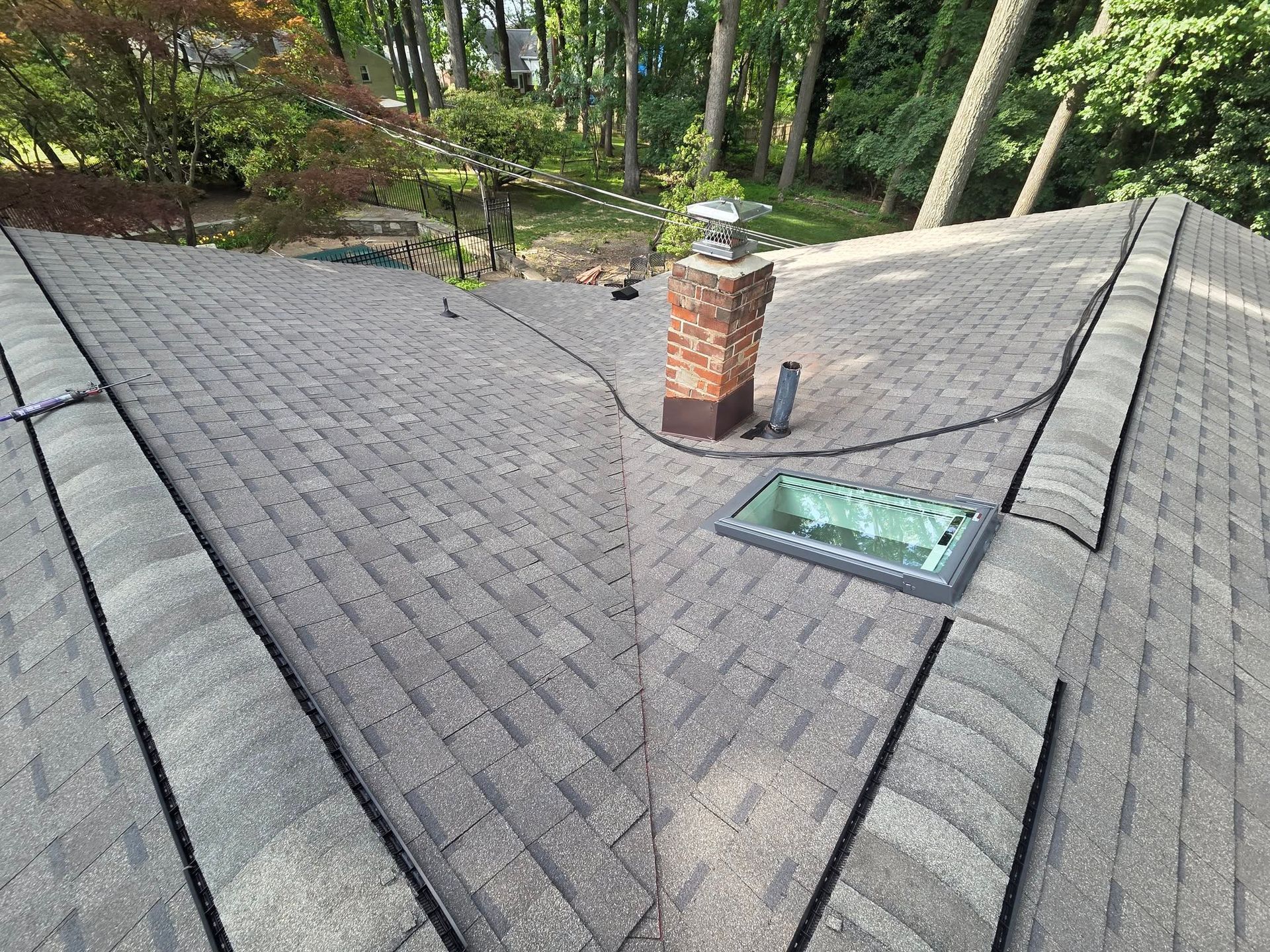 Roof with gray shingles, brick chimney, skylight, and trees in the background