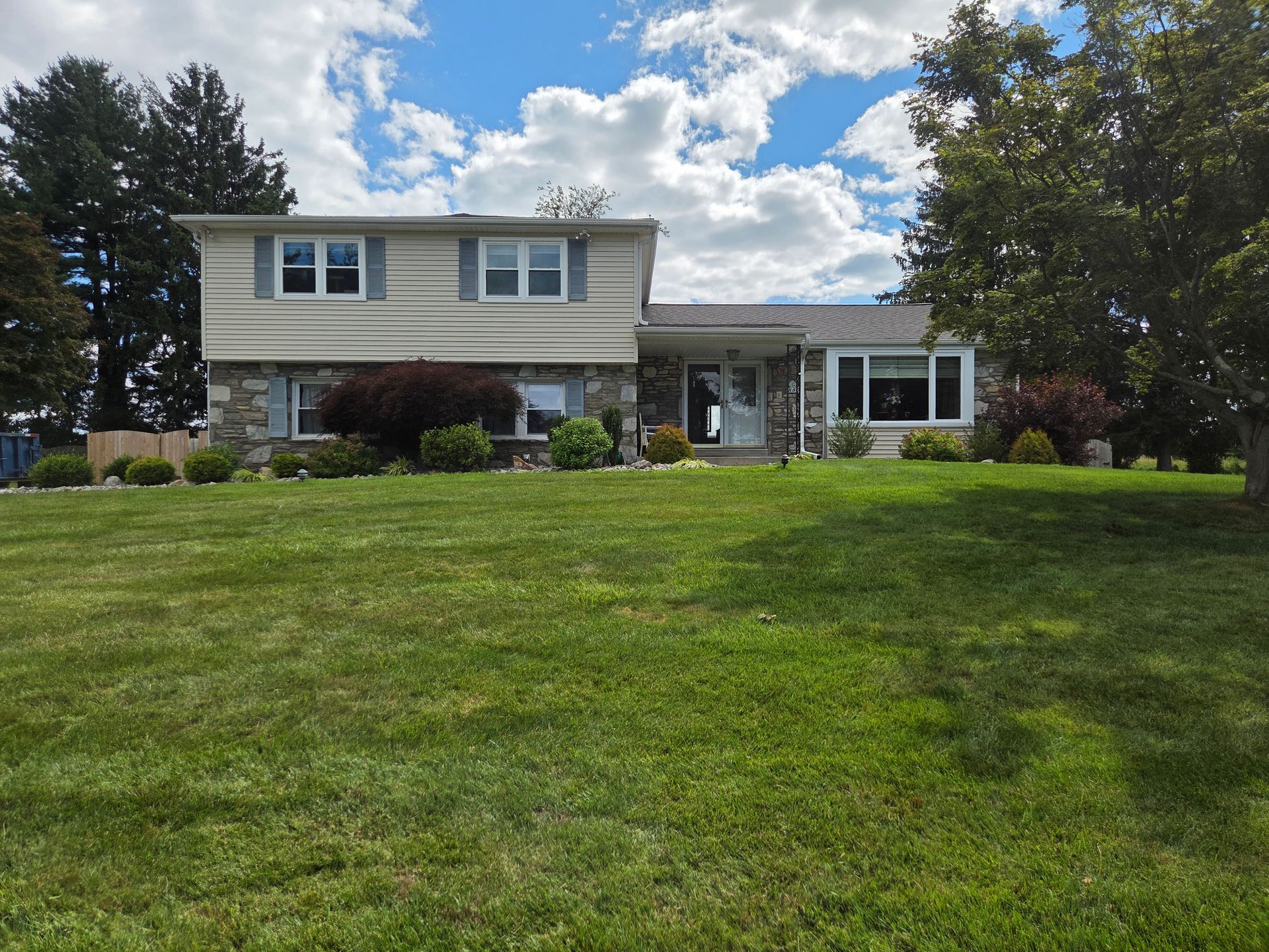 Suburban two-story house with a large green lawn under a partly cloudy sky