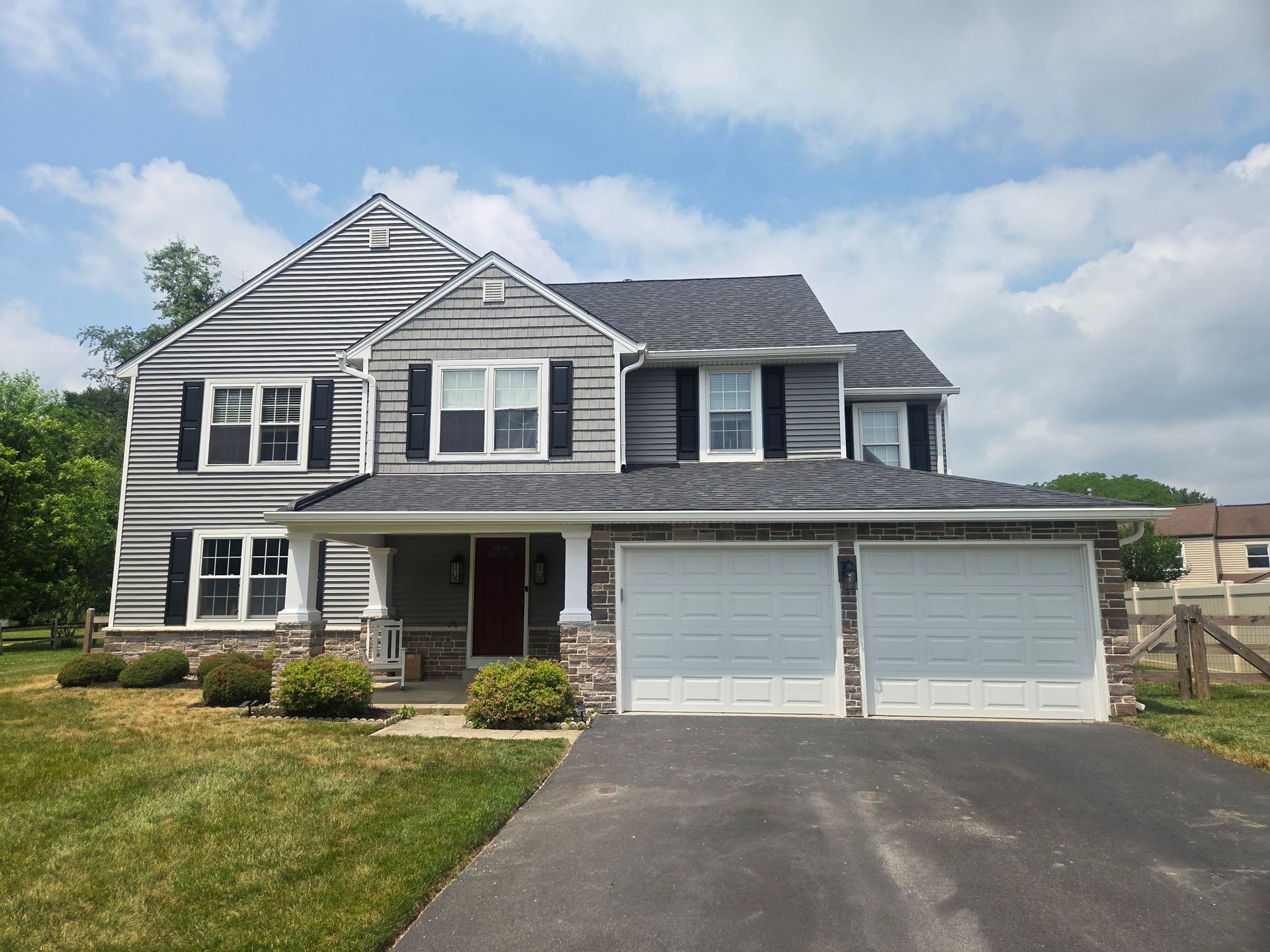 Two-story gray house with white trim, front porch, and double garage under a partly cloudy sky