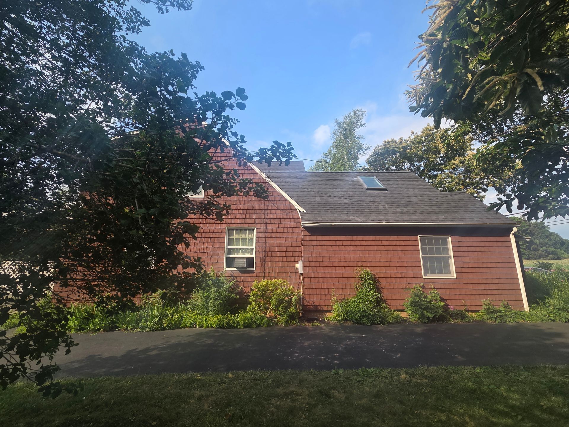 Red house with gray roof and skylight, framed by trees under a blue sky.