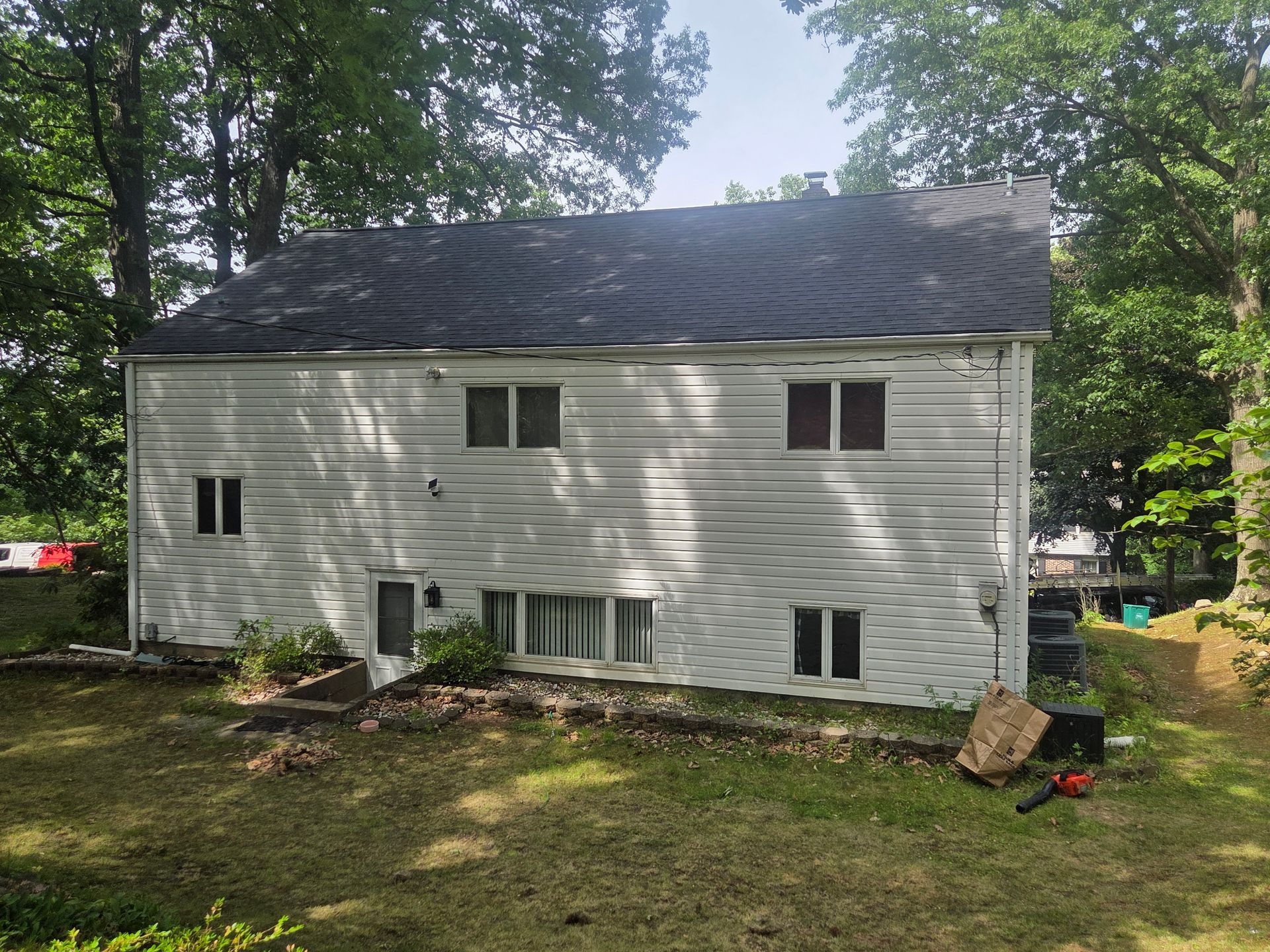 White two-story house in wooded yard with scattered debris and a damaged lower wall
