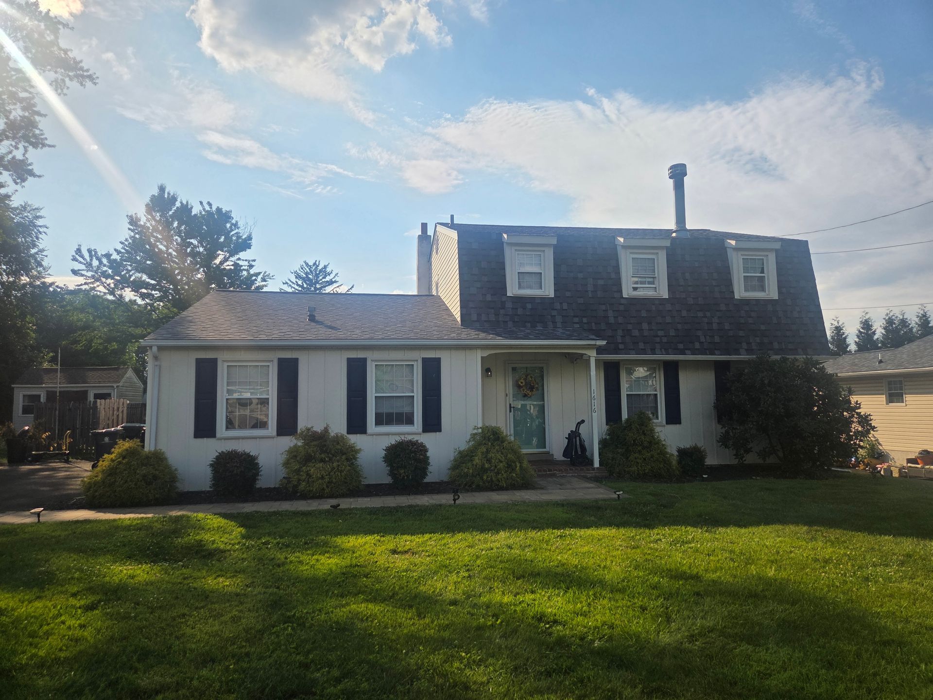 Two-story white house with dark shutters and a green lawn in bright sunlight