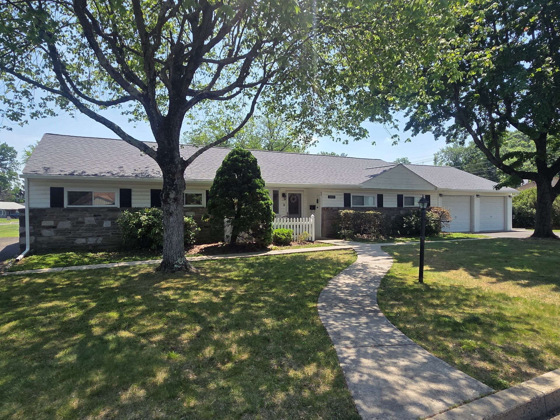 Suburban single-story house with a curved walkway, large trees, and a shaded front lawn.