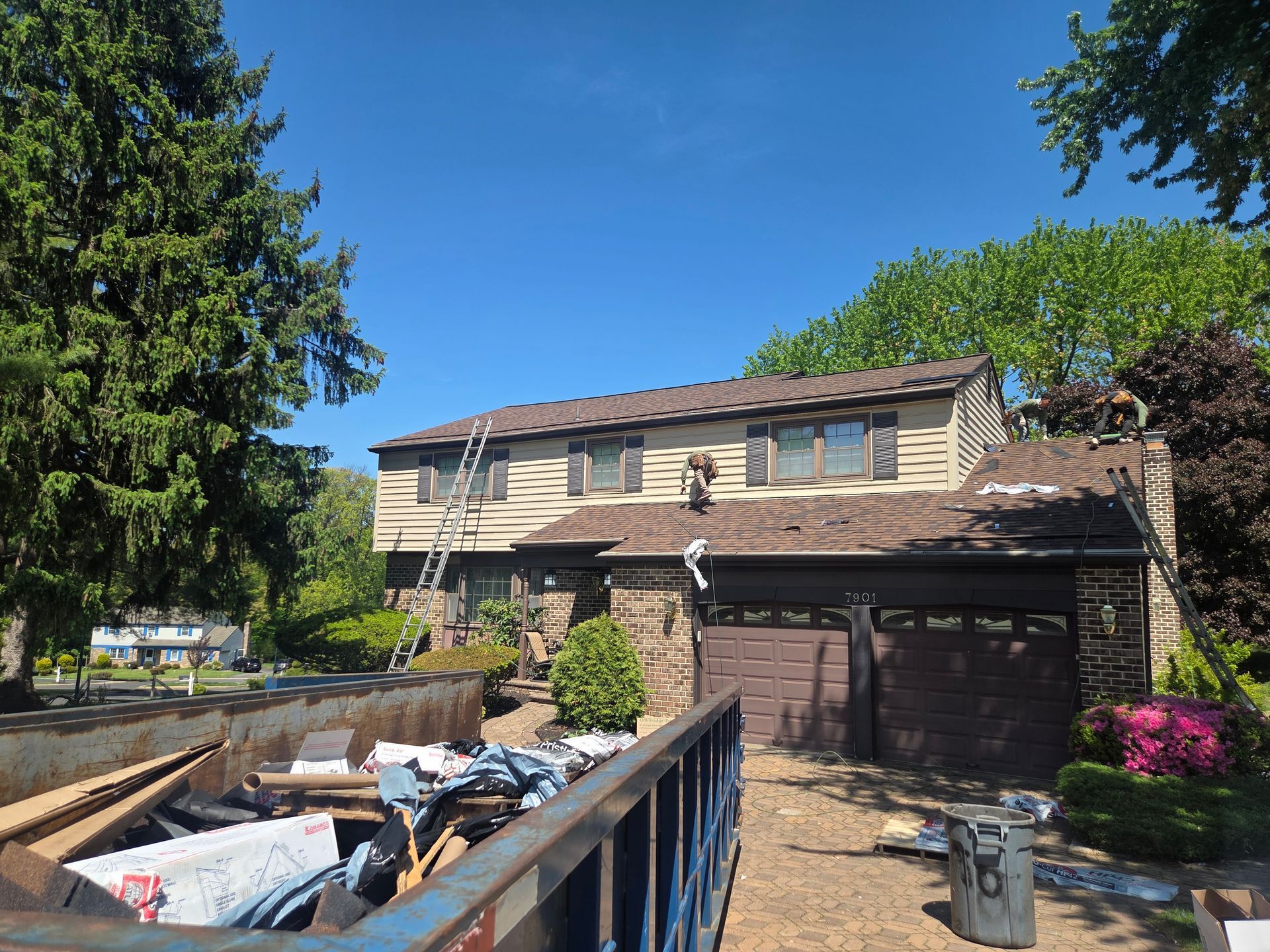 Suburban house with attached garage, driveway debris bin, and blue sky on a sunny day