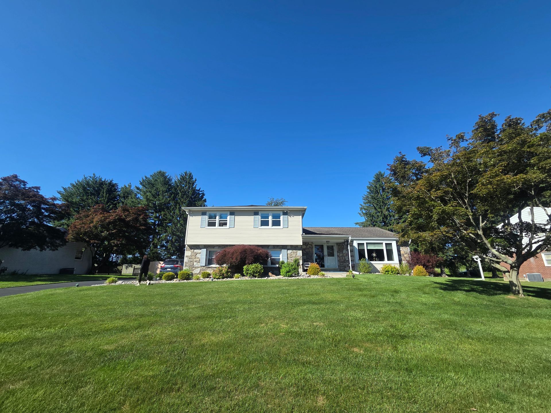 Suburban two-story house with a large green lawn under a clear blue sky
