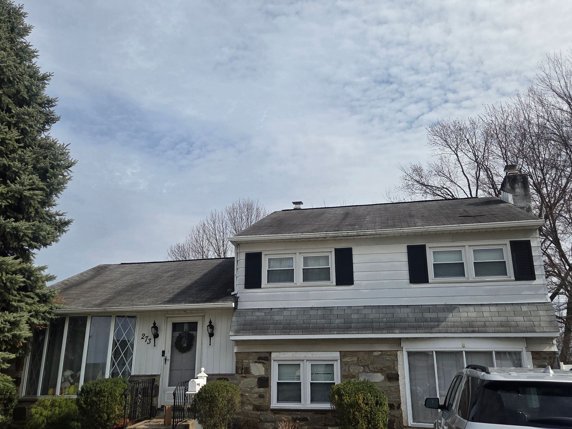 Two-story white house with a front porch, gray roof, and a parked SUV under a cloudy sky
